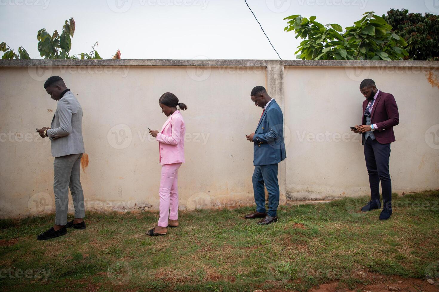 a group of well-dressed young Africans use their smartphones in line while keeping a safe distance during the pandemic. photo