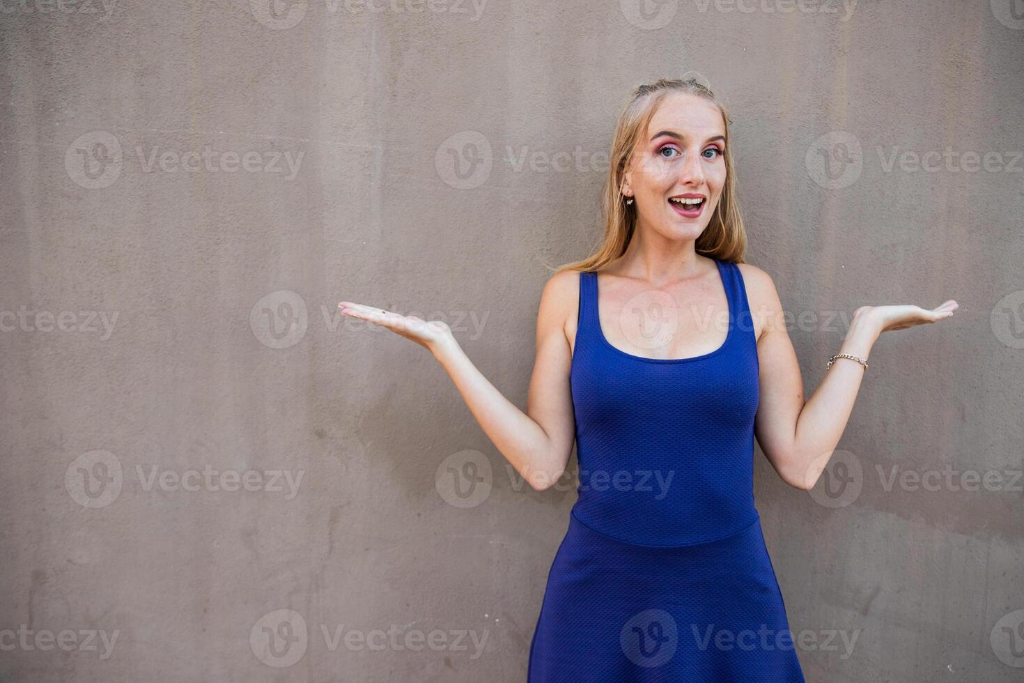 Attractive woman with surprised expression and raised arms, model isolated on grey background photo
