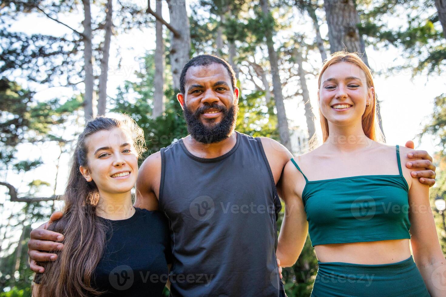 Three sporty people are standing in a forest, smiling and posing for a picture during a training photo