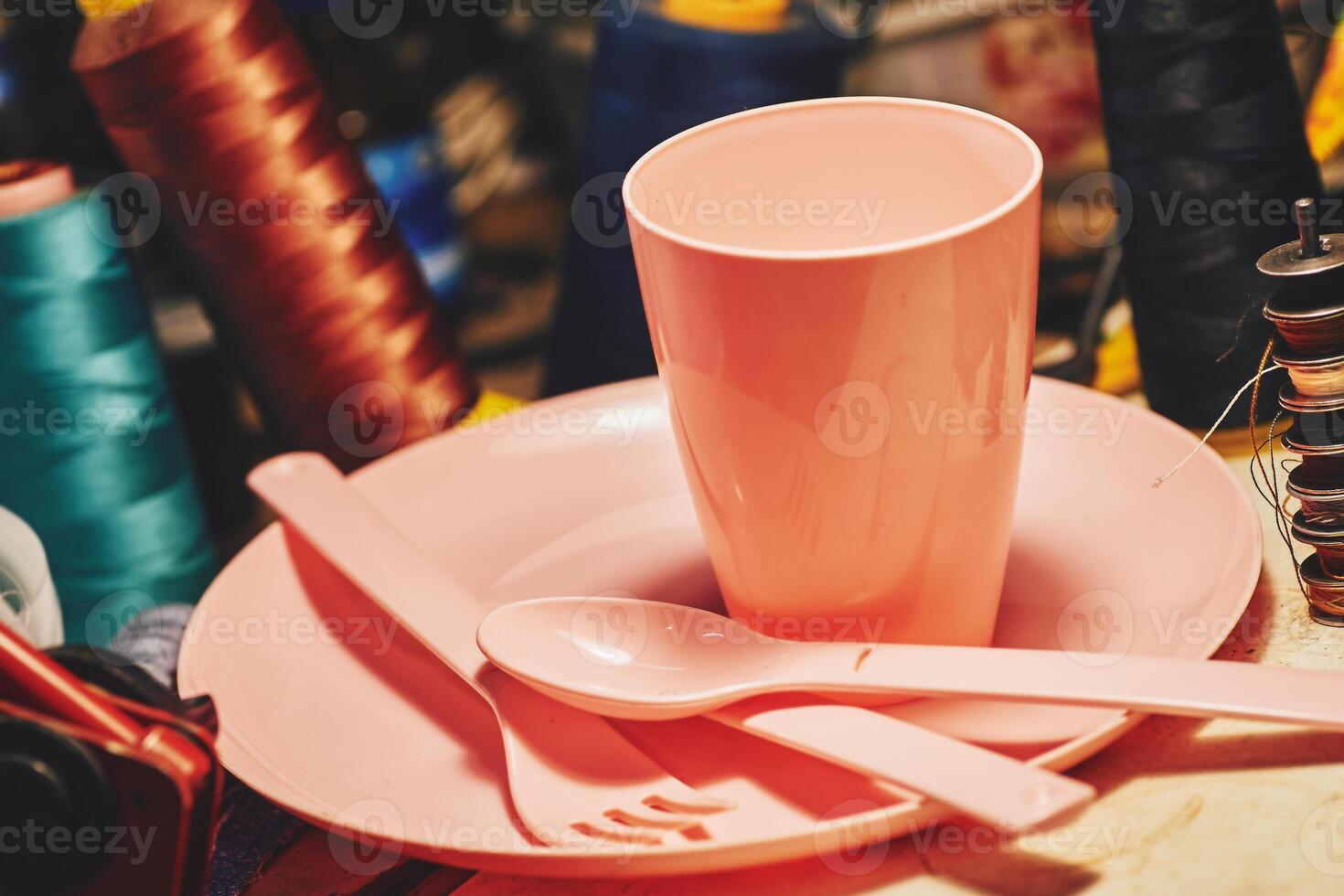 Pink plastic dinnerware set in tailor sewing workshop.Cup,fork,knife,spoon photo