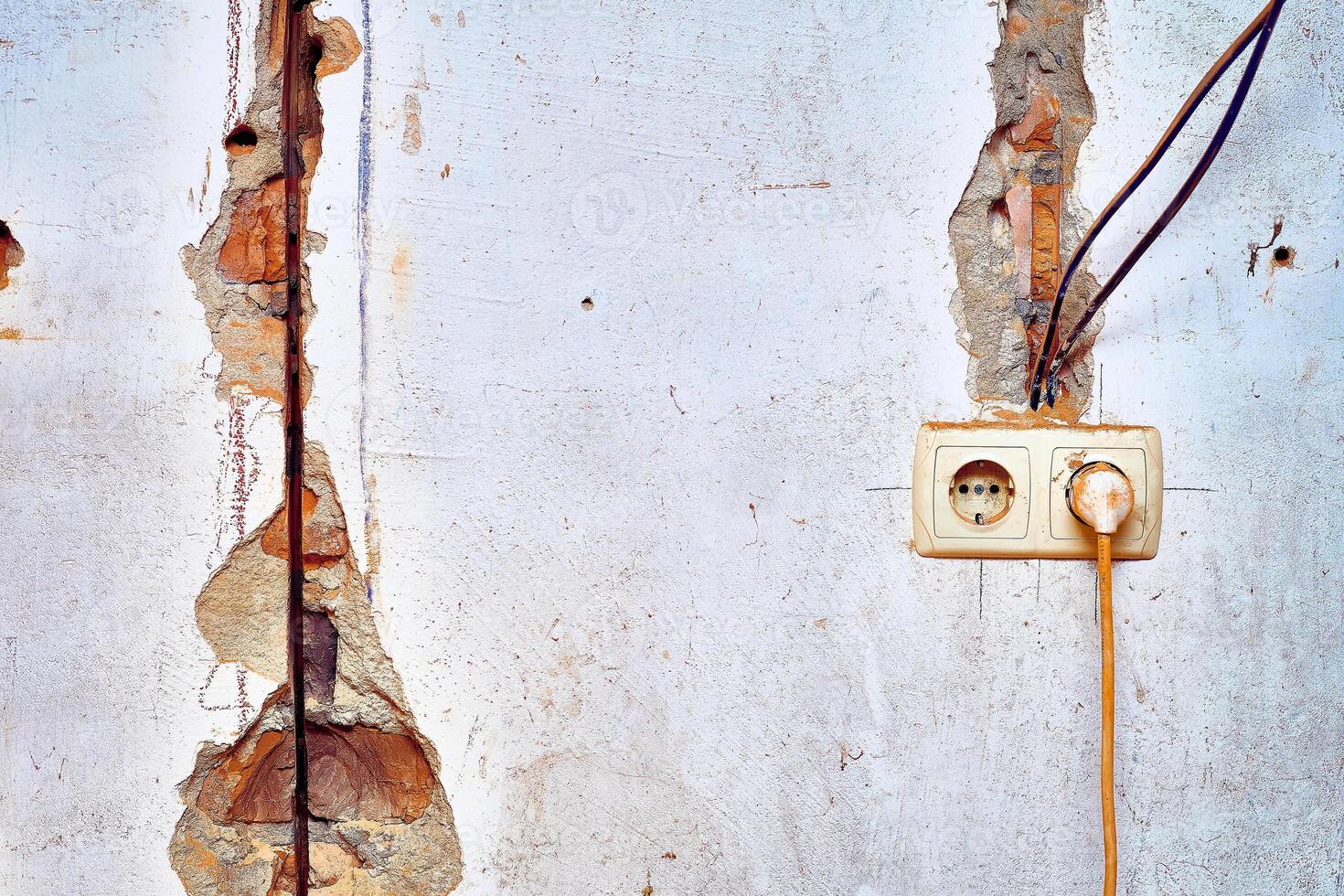 Old brick wall before renovation. Connected socket, wiring, cracks photo