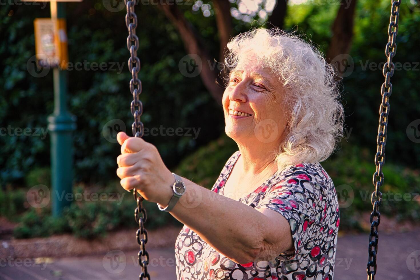 An elderly lady in the park is holding on to the chain of a swing. photo