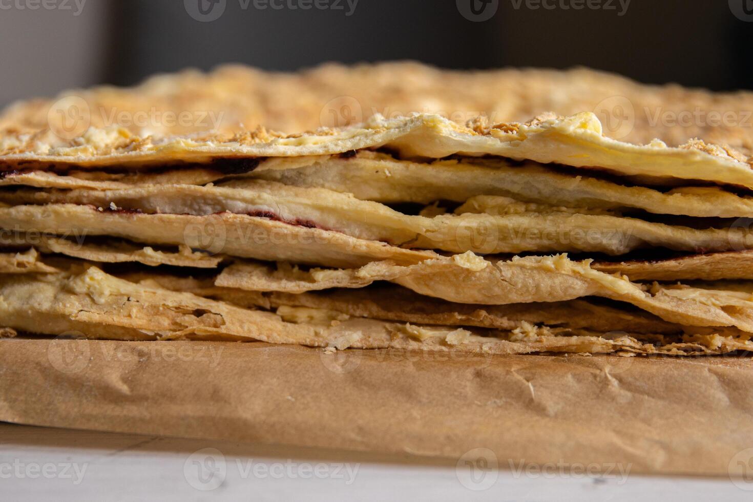 Backing process. Closeup of Puff pastry layers of the delicious French Napoleon cake laying on the backing paper. French pastry with custard butter cream. Side view. Selective focus. photo
