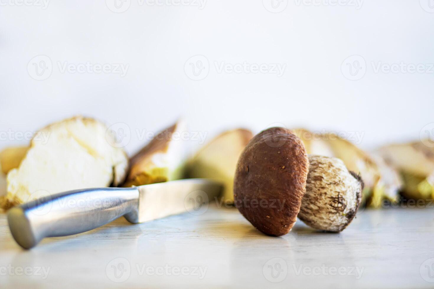 Cutting white mushrooms with knife into many slices on wooden kitchen board or table. Cooking fungus. Knife cuts boletus fungi. Dividing into parts. Minimalist design concept. Close up. Copy space photo