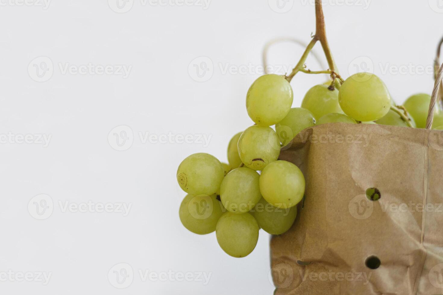 Close up of a bunch of green grapes in a paper shopping bag. Fresh bunches of white grapes in a ecological package, isolated on white background. Healthy fruits concept. Copy space. Selective focus photo