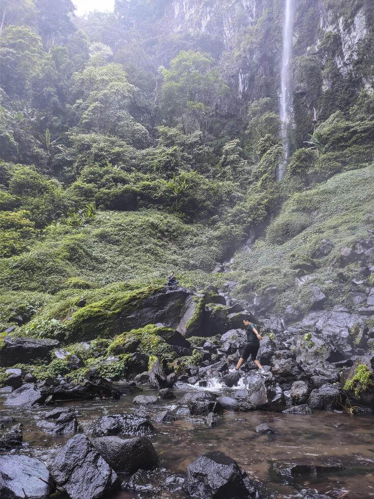 a man standing in a stream near a waterfall photo