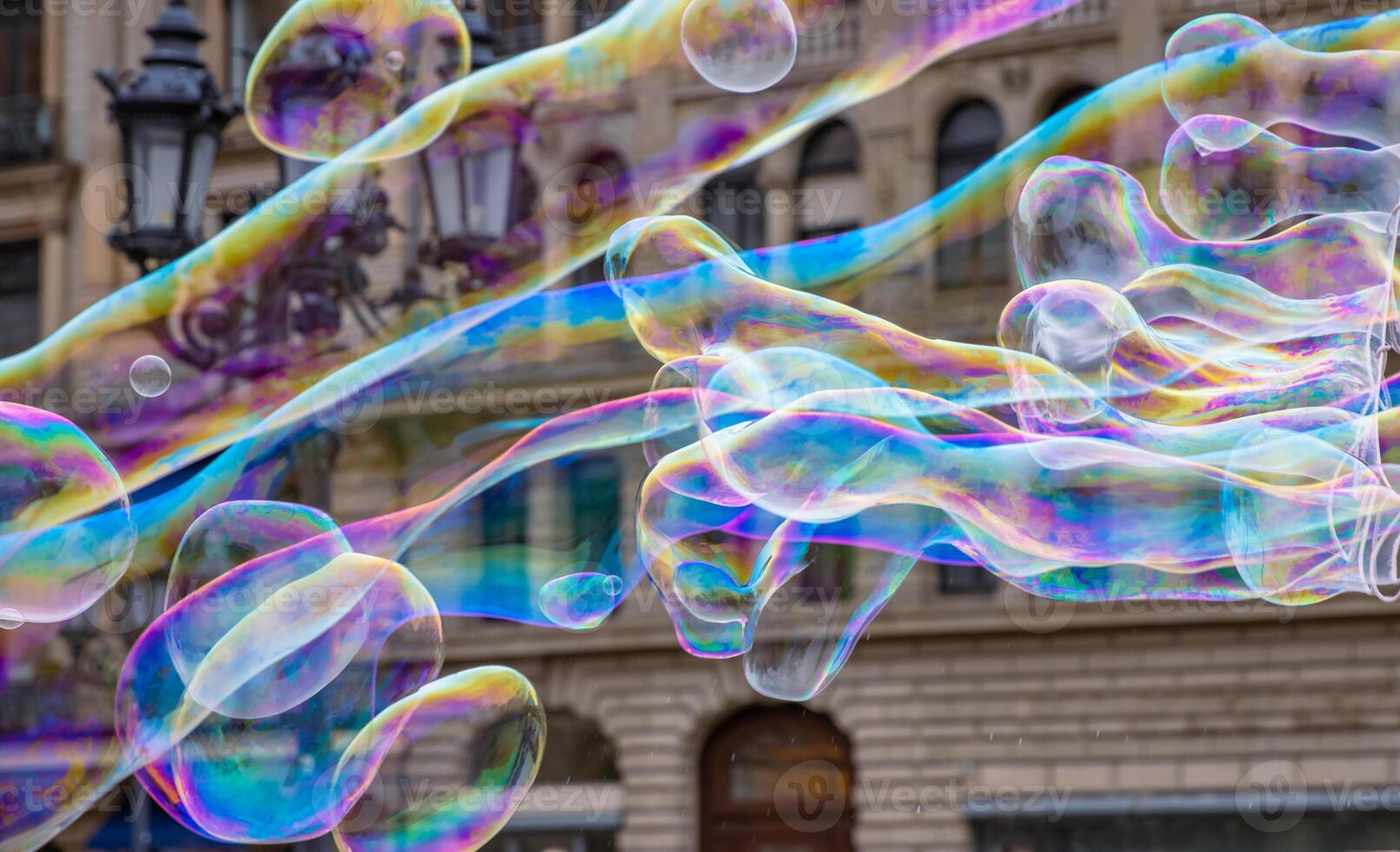 Many multicolored giant soap bubbles flying in the air on a windy day. Huge bubble are stretching on the wind into long smoothy changing form without popping. Close up. Copy space. Selective focus. photo