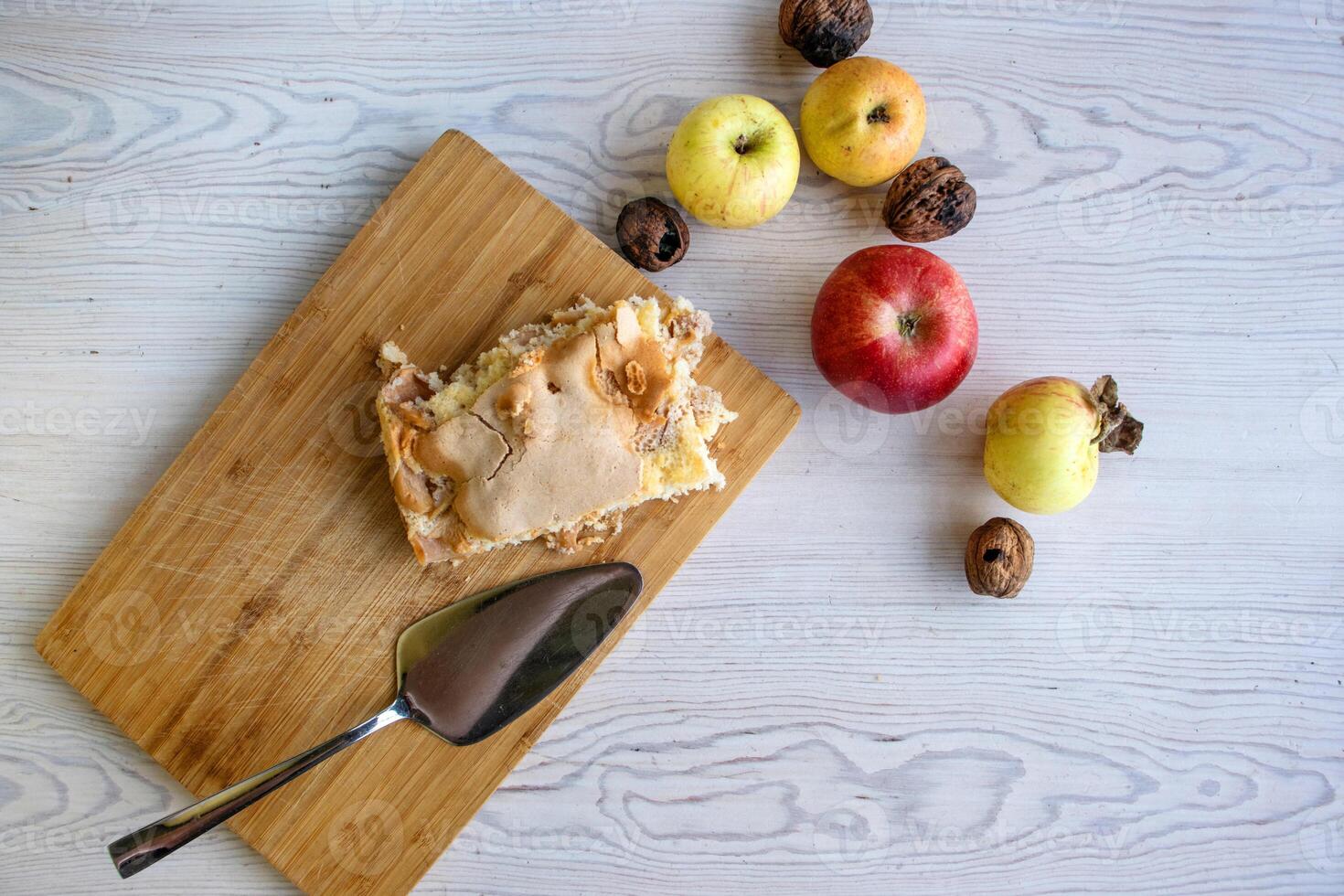 Piece of traditional thanksgiving apple cinnamon pie on the wooden cutting board with apples and walnuts on the white table. Homemade baked fruit tart with golden crust. Close up, copy space, top view photo
