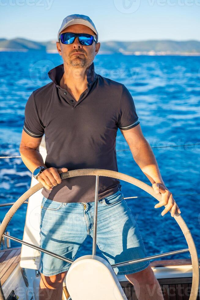 Young man captain stands at the helm and controls a sailboat during a journey by sea. High quality photo