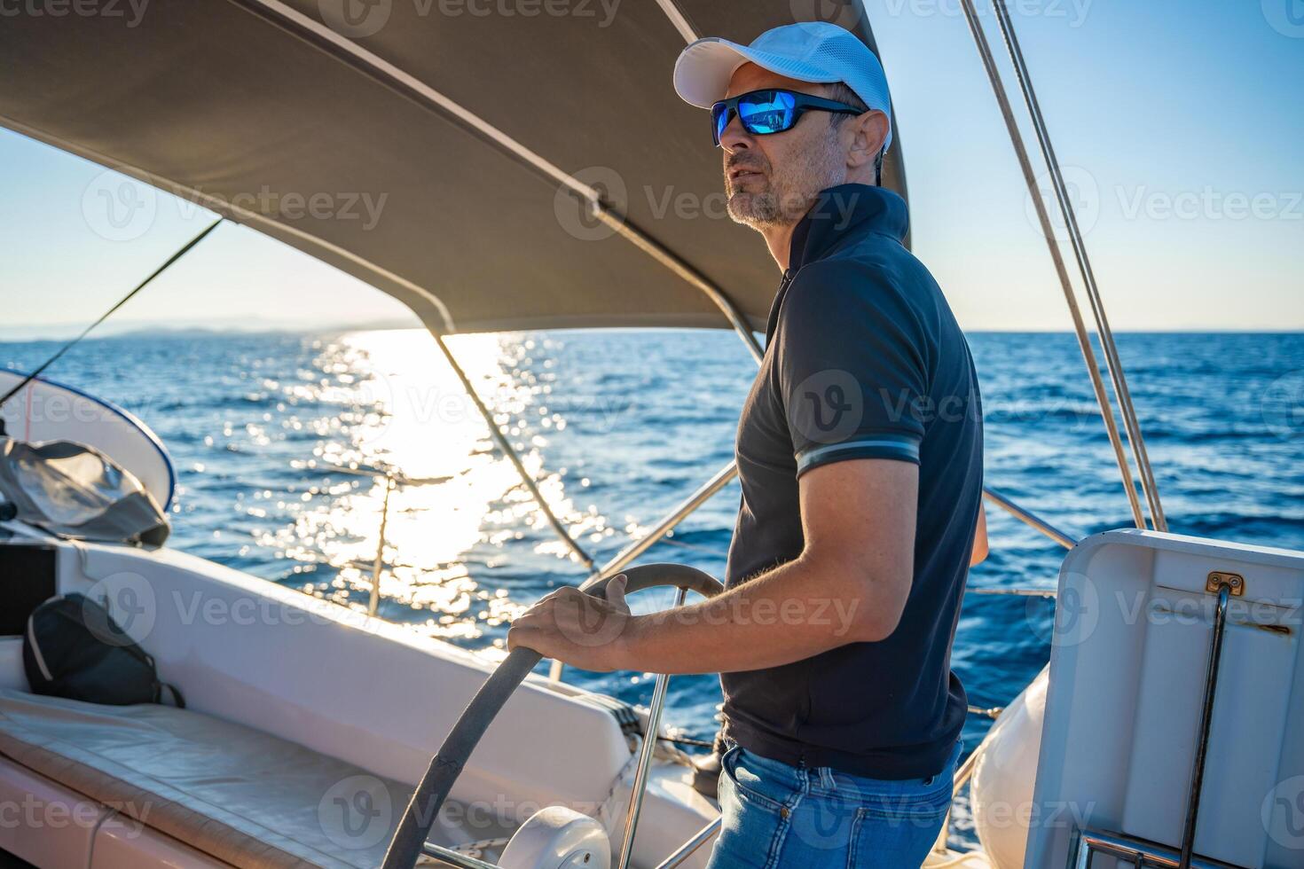 Young man captain stands at the helm and controls a sailboat during a journey by sea. High quality photo