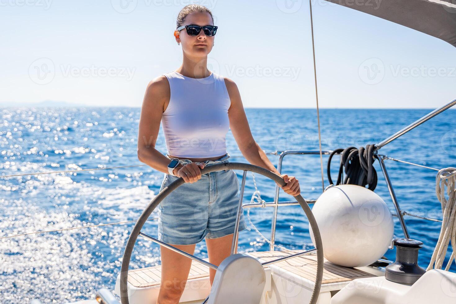 Young woman female captain stands at the helm and controls a sailboat during a journey by sea. High quality photo