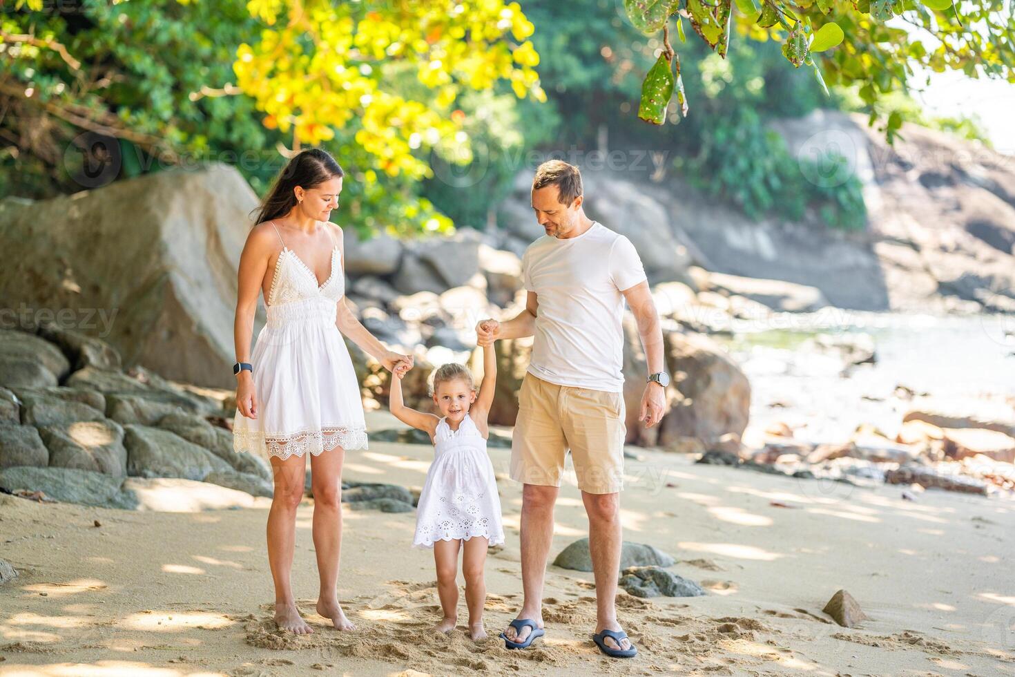 Happy young family of three taking a walk on the beach, having a fun on seashore in the shade of trees and palms. Happy family concept. photo