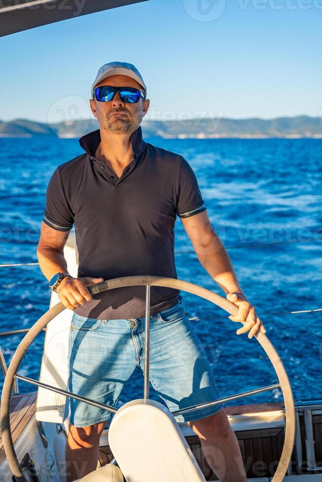 Young man captain stands at the helm and controls a sailboat during a journey by sea. High quality photo