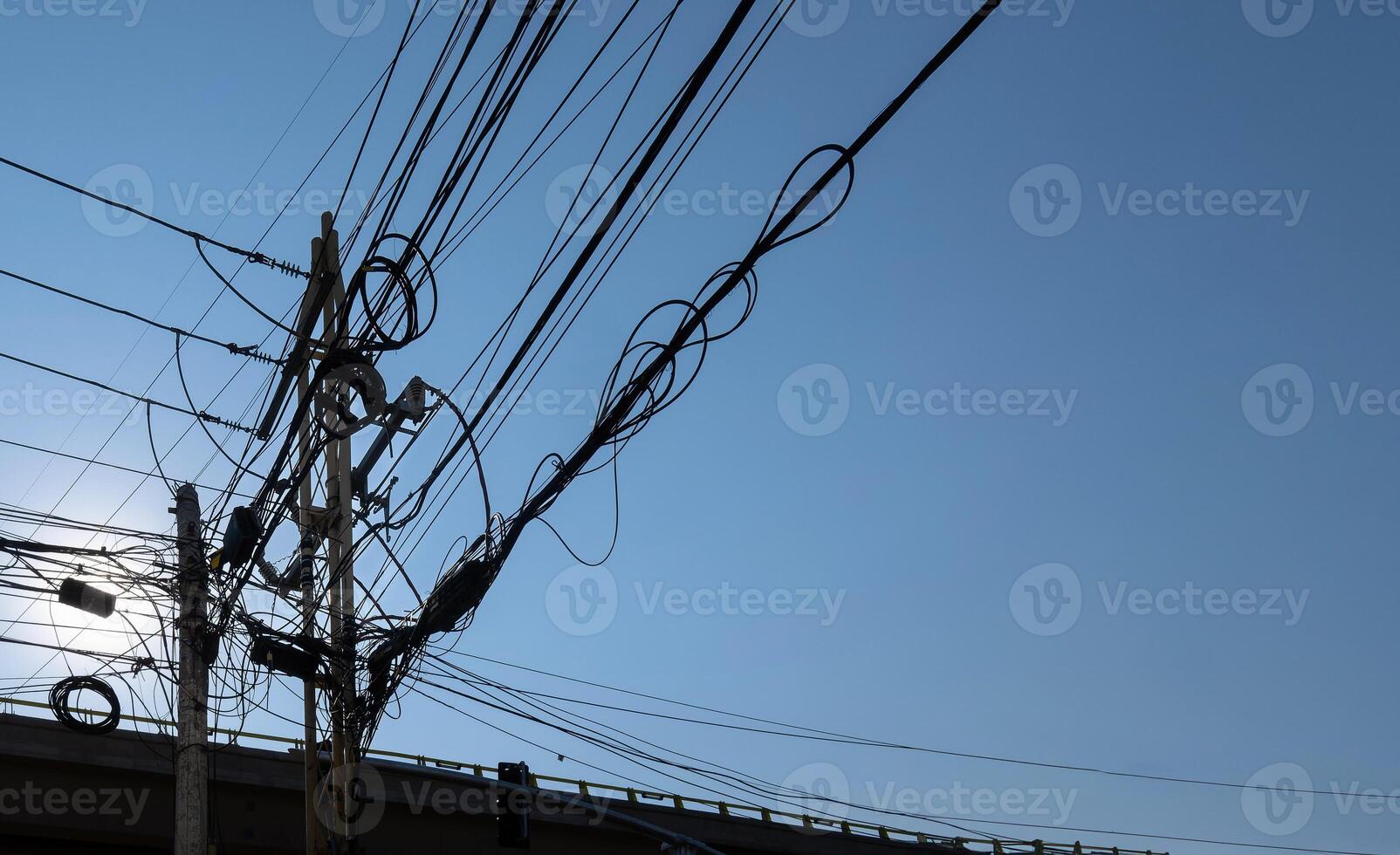 Intricate Network of Power Lines Against a Clear Blue Sky with Overpass in Background photo