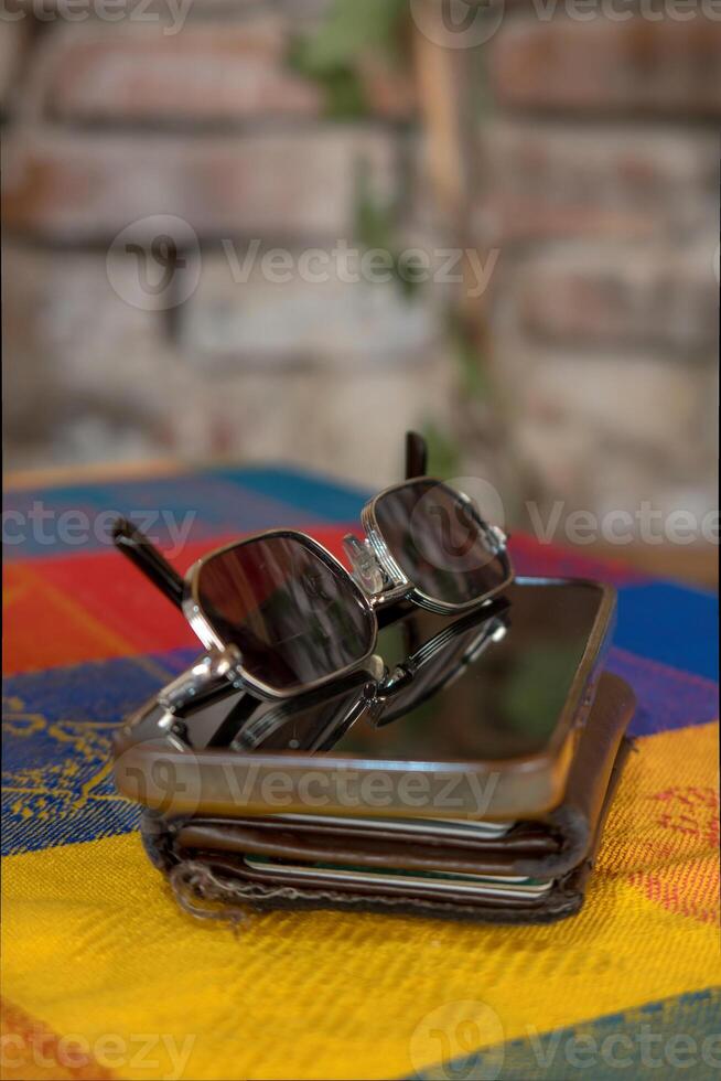 Stylish Sunglasses and Smartphone on Wallet Against Rustic Brick Wall photo