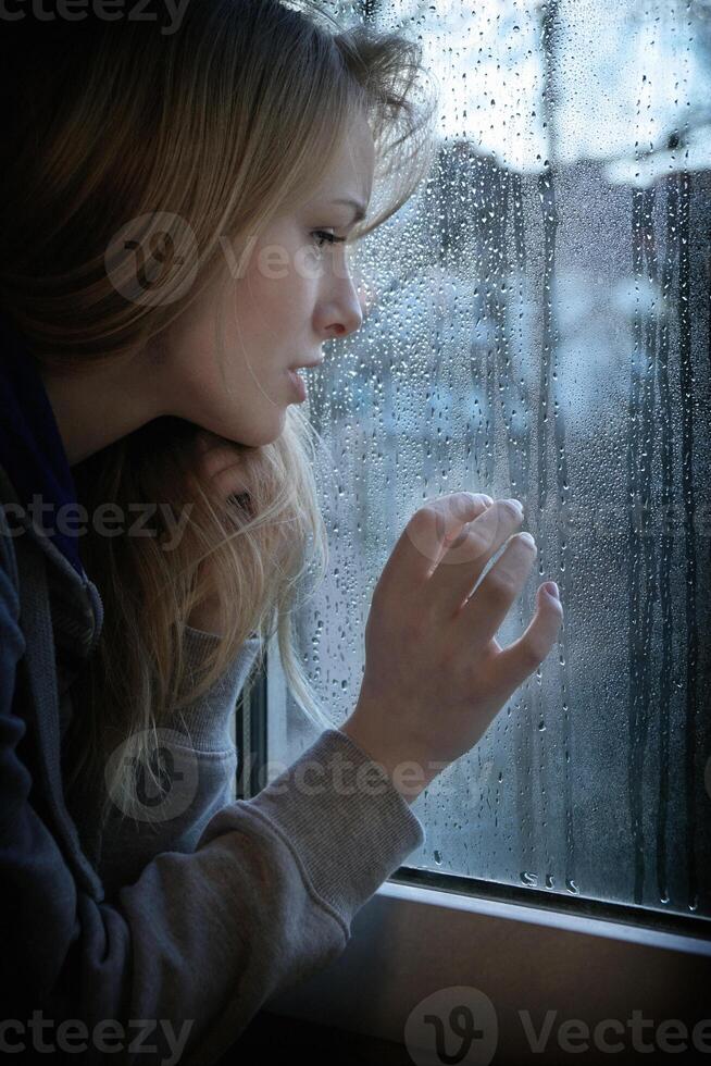 woman looking through window with raindrops photo