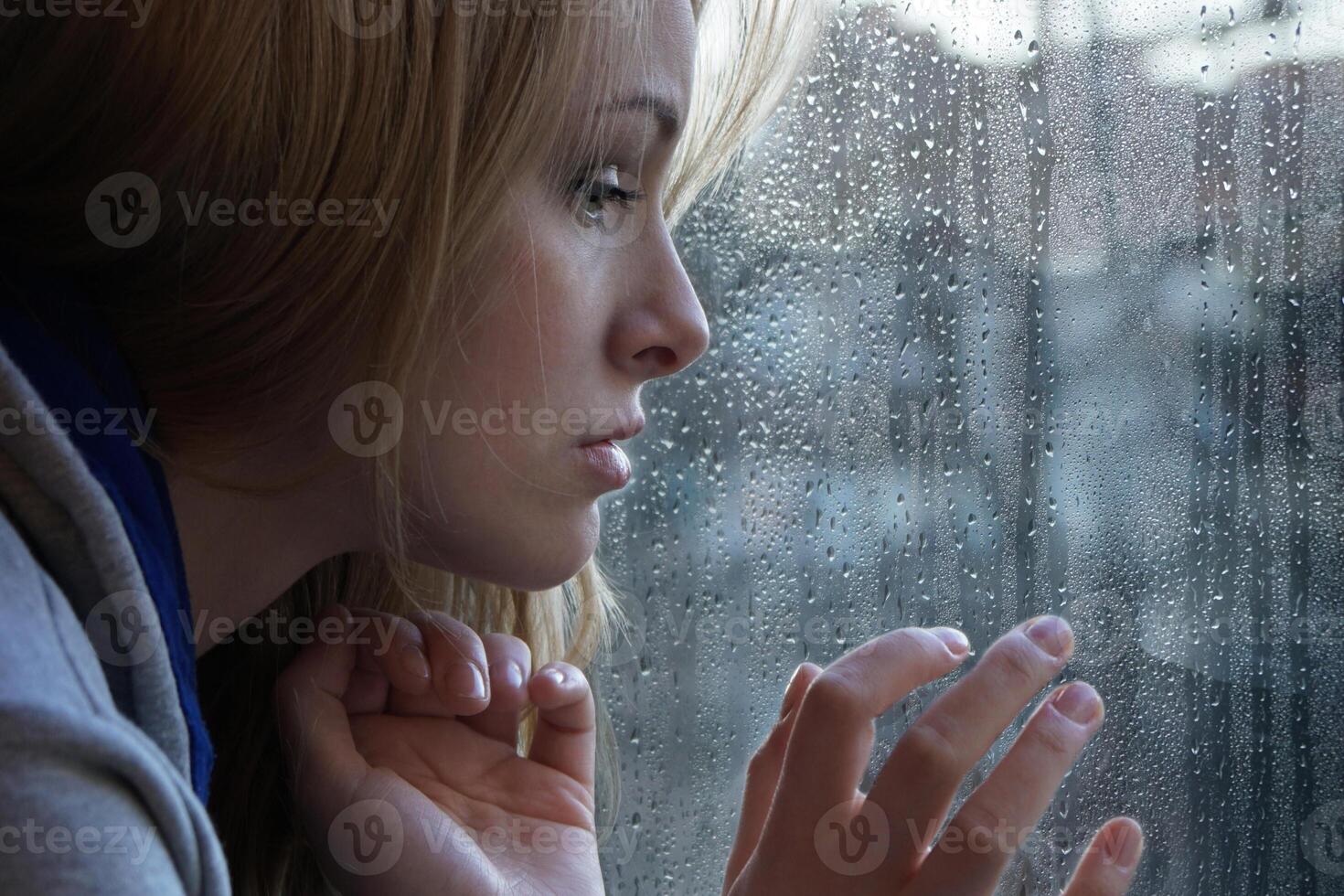 sad young woman looking through window on rainy day photo