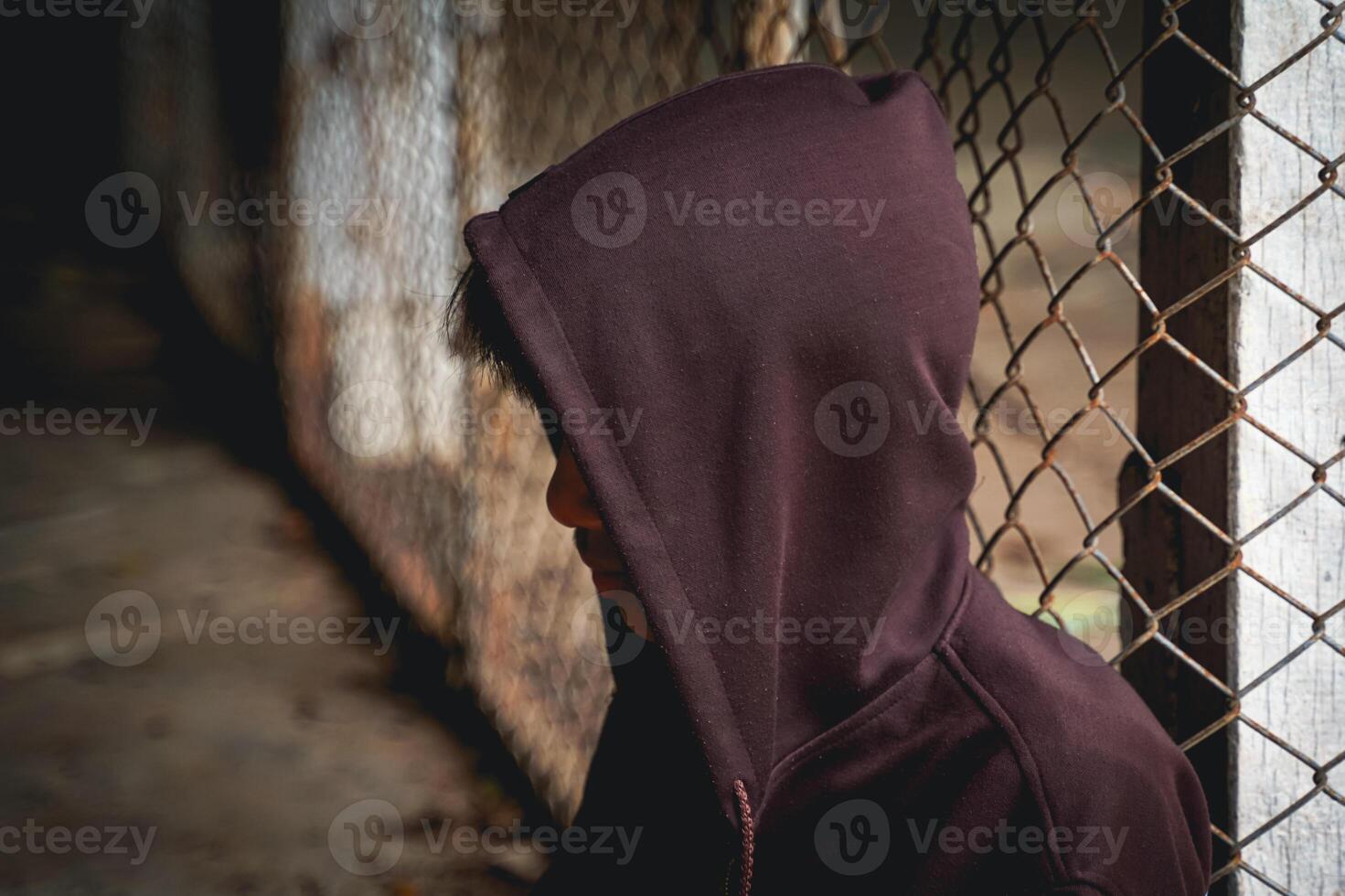 Thai male teenager wearing a hoodie Covering his face, he sat sadly alone with his back against the steel wall of the detention center. photo