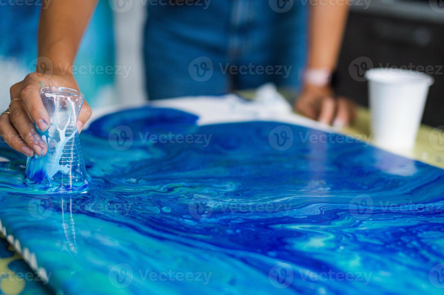 Person creating blue acrylic pour art on canvas. Art and creativity concept. photo