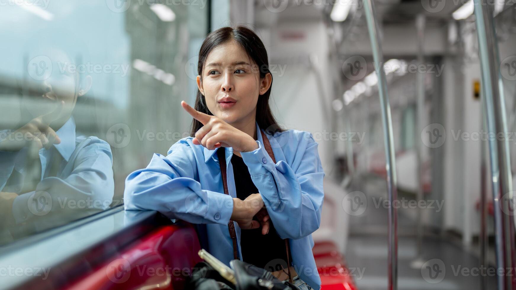 A cheerful Asian woman is enjoying the view outside while sitting on a seat in a sky train. photo