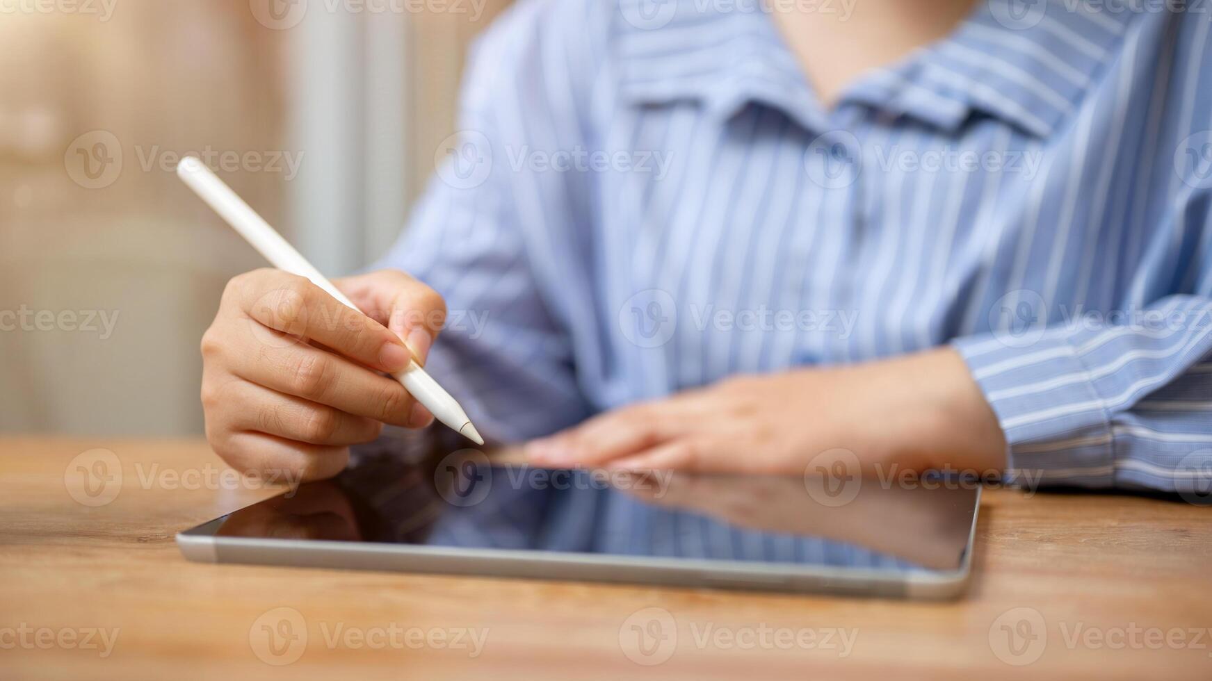 A cropped image of an Asian woman holding a stylus pen and using her digital tablet in a coffee shop photo