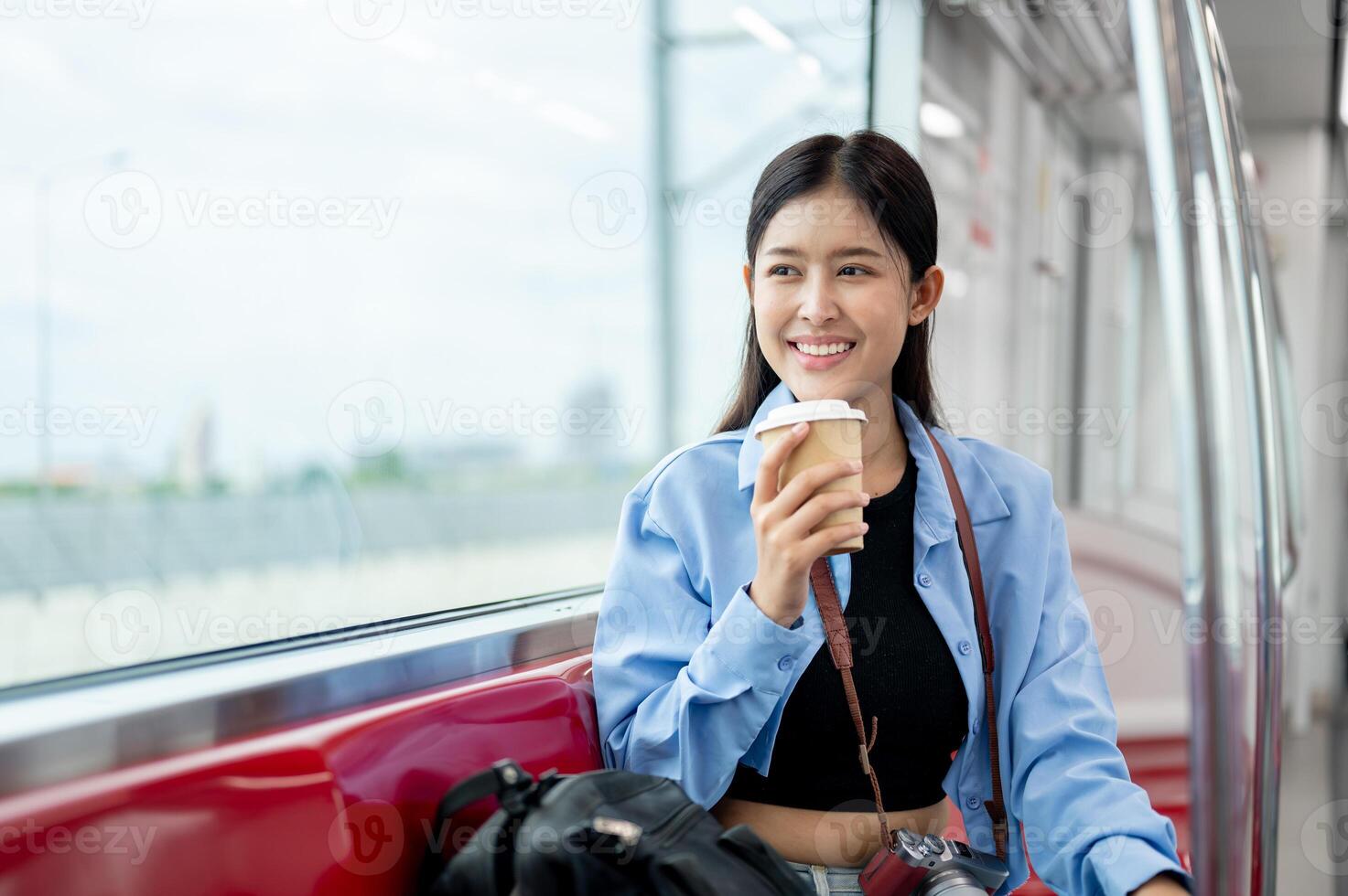 A happy Asian female passenger is sipping coffee while enjoying the view outside of a sky train. photo