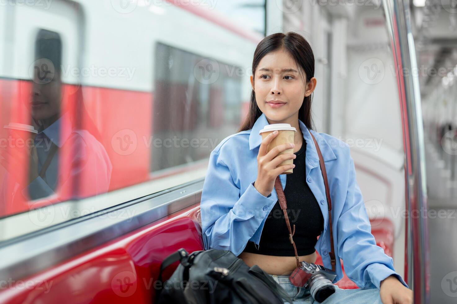A happy Asian female passenger is sipping coffee while enjoying the view outside of a sky train. photo