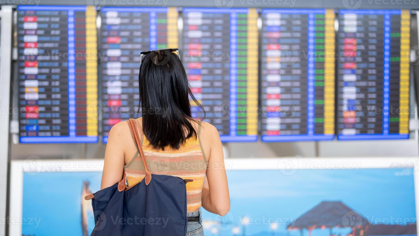 An Asian female tourist standing in front of a flight information display in the airport terminal. photo