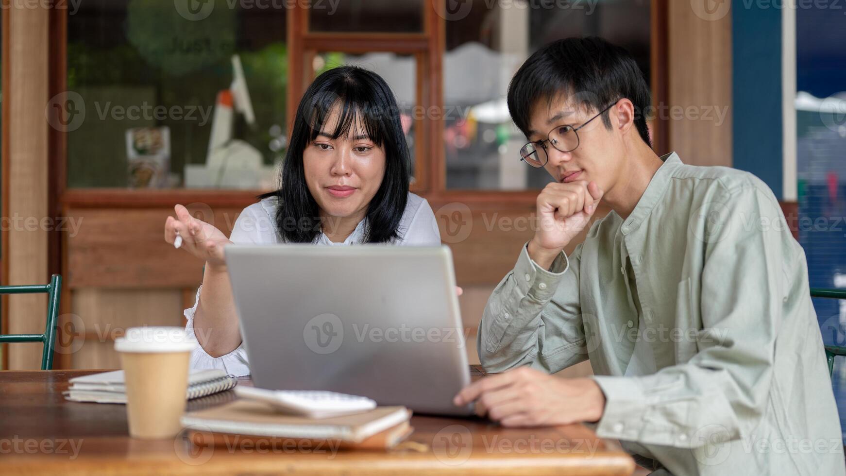 Two positive Asian male and female friends are brainstorming and discussing work at a cafe. photo