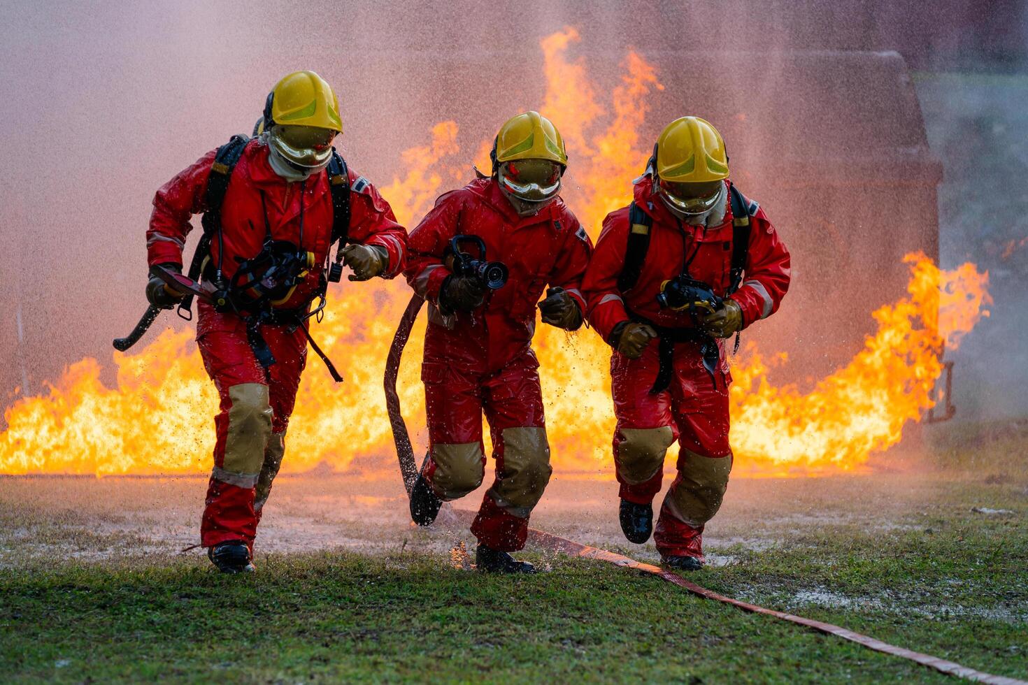 Three firefighters are running through a fire, one of them holding a hose photo