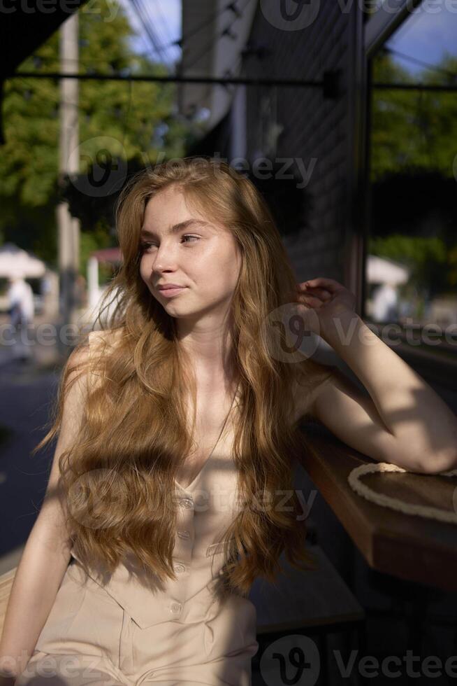 a beautiful teenage girl in a peach fuzz suit with a waistcoat in the old money style sits at the bar outside photo