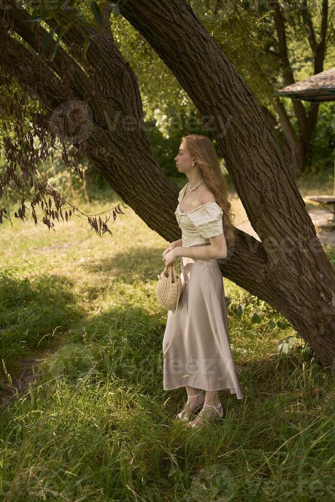 beautiful teenage girl in a silk skirt and a corset in the old money style walks in the park and along the river bank photo