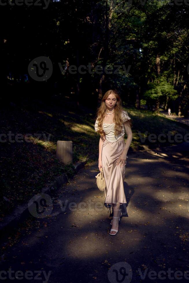 beautiful teenage girl in a silk skirt and a corset in the old money style walks in the park and along the river bank photo