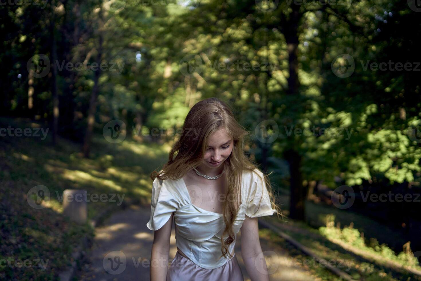 beautiful teenage girl in a silk skirt and a corset in the old money style walks in the park and along the river bank photo