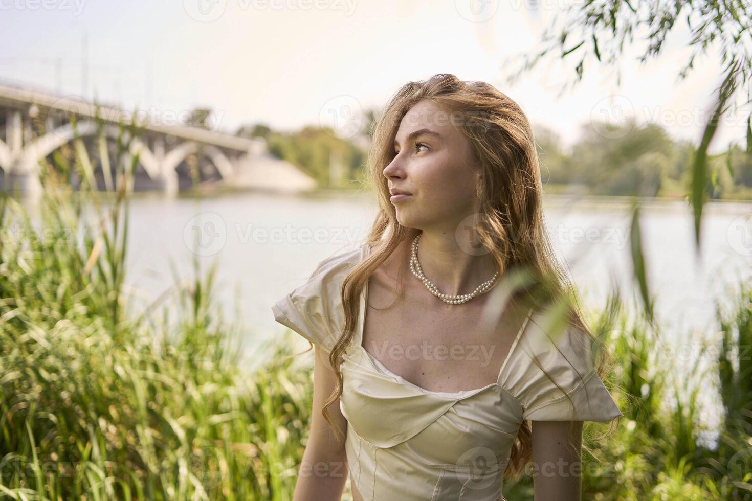 beautiful teenage girl in a silk skirt and a corset in the old money style walks in the park and along the river bank photo