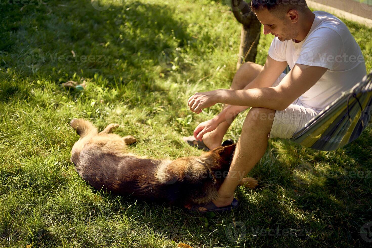 man rests and listens to music in a hammock, his dog rests nearby photo