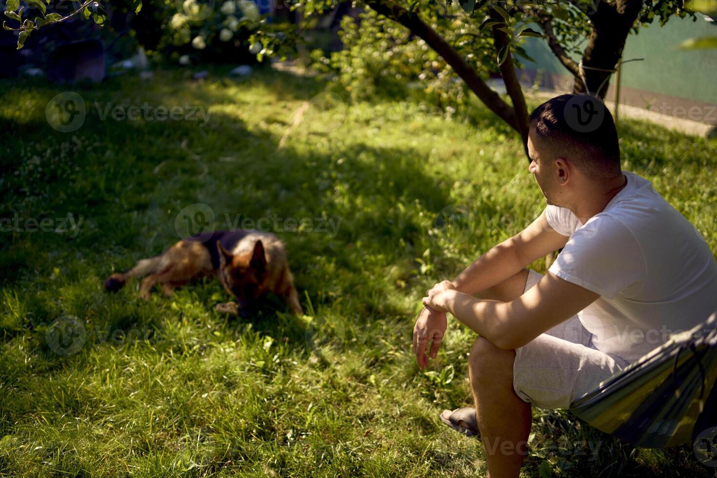 man rests and listens to music in a hammock, his dog rests nearby photo