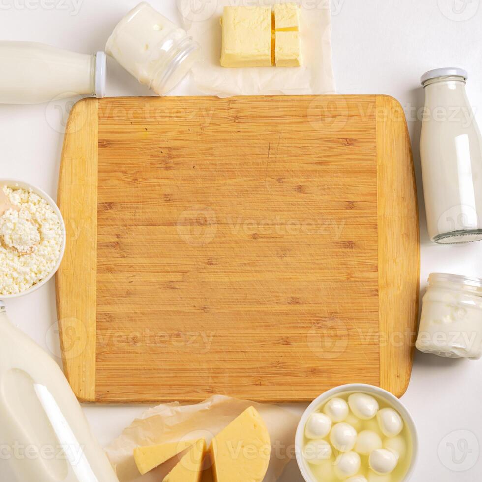 Dairy and sour-milk fermented organic products are laid out in a frame near cutting wooden board on a white background. photo