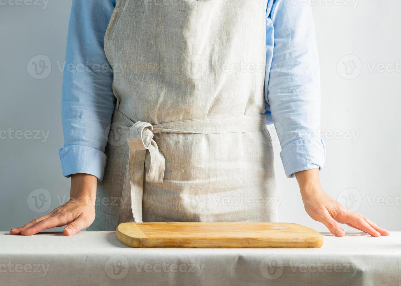 Female cook in cotton apron at the kitchen table with cutting board. Rustic natural style. Kinfolk concept. Copy space. photo