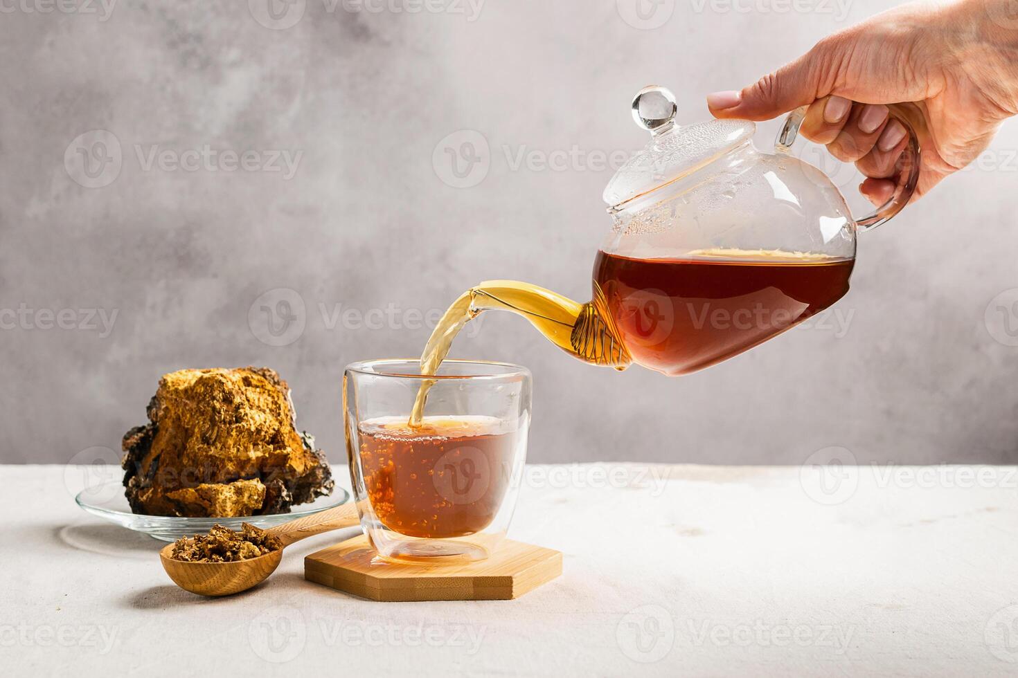 A female hand pours tea from glass teapot from birch chaga mushrooms. Organic drink antioxidant gray natural background. photo