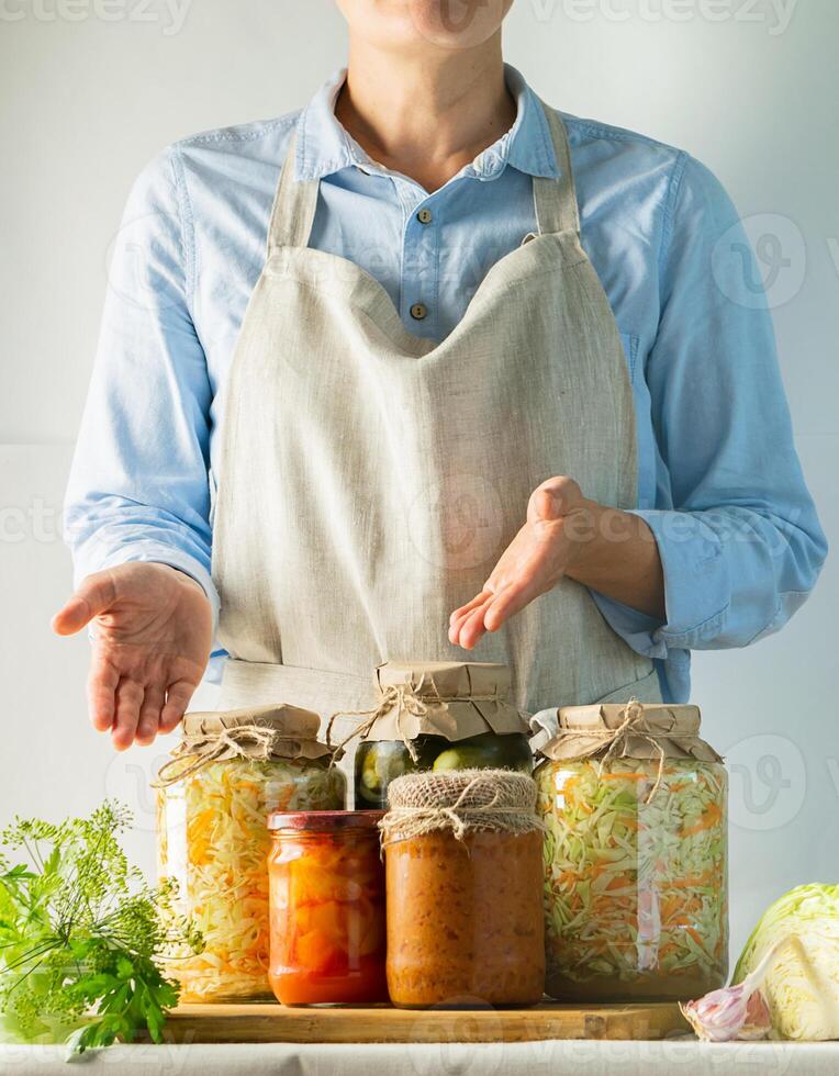 Fermented and canned vegetables various cans stand on the table and a woman cook in an apron. Recycling Autumn Harvest photo