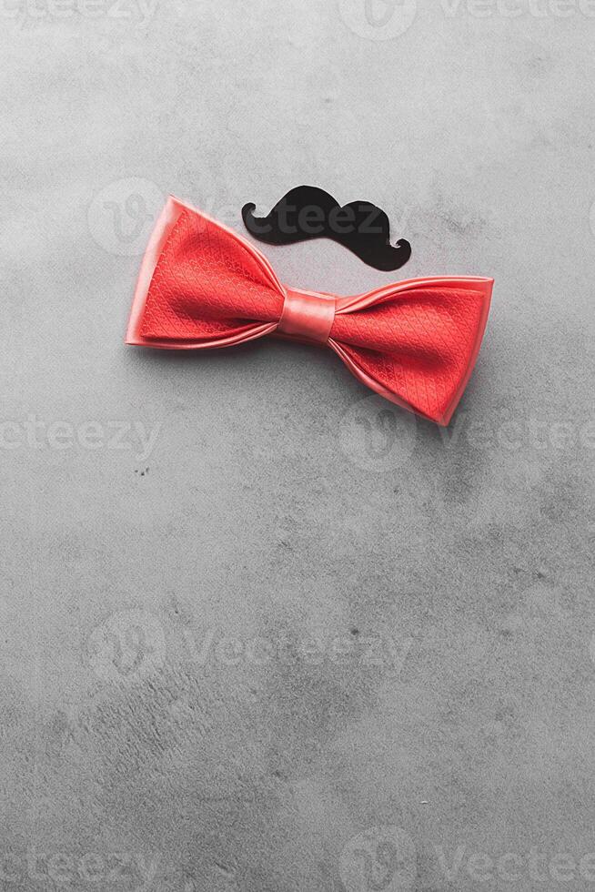 Decorative black mustache and red bow-tie on a gray background. The concept of men's holiday father's day. Top view photo