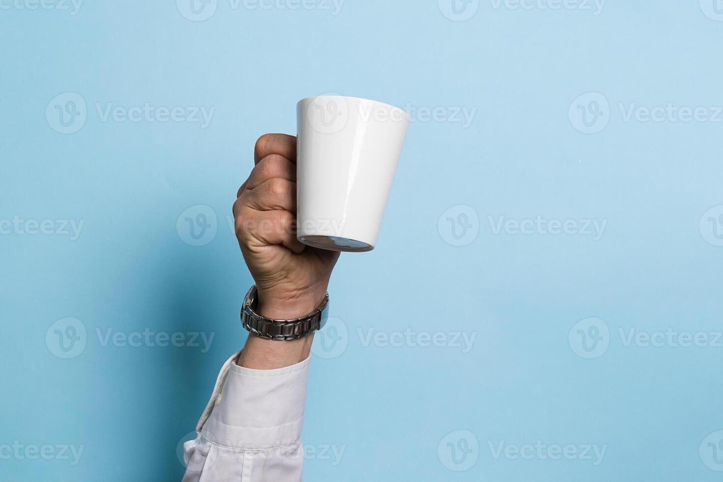 A man holds a cup of coffee or tea drink high in his hand a blue background. Food drink concept. Copy space photo