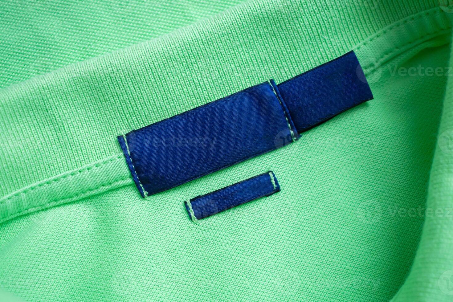 Blank blue laundry care clothes label on green shirt fabric texture background photo