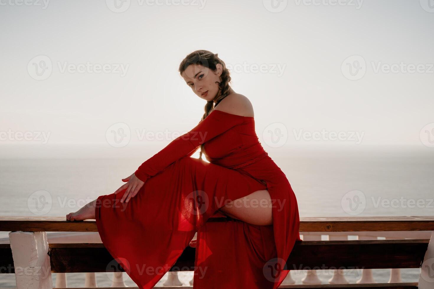 Closeup portrait of sensual young brunette woman in red dress, happily dancing outdoors isolated on blurry sea background with natural bokeh in soft warm sunset backlight. Selective focus. photo