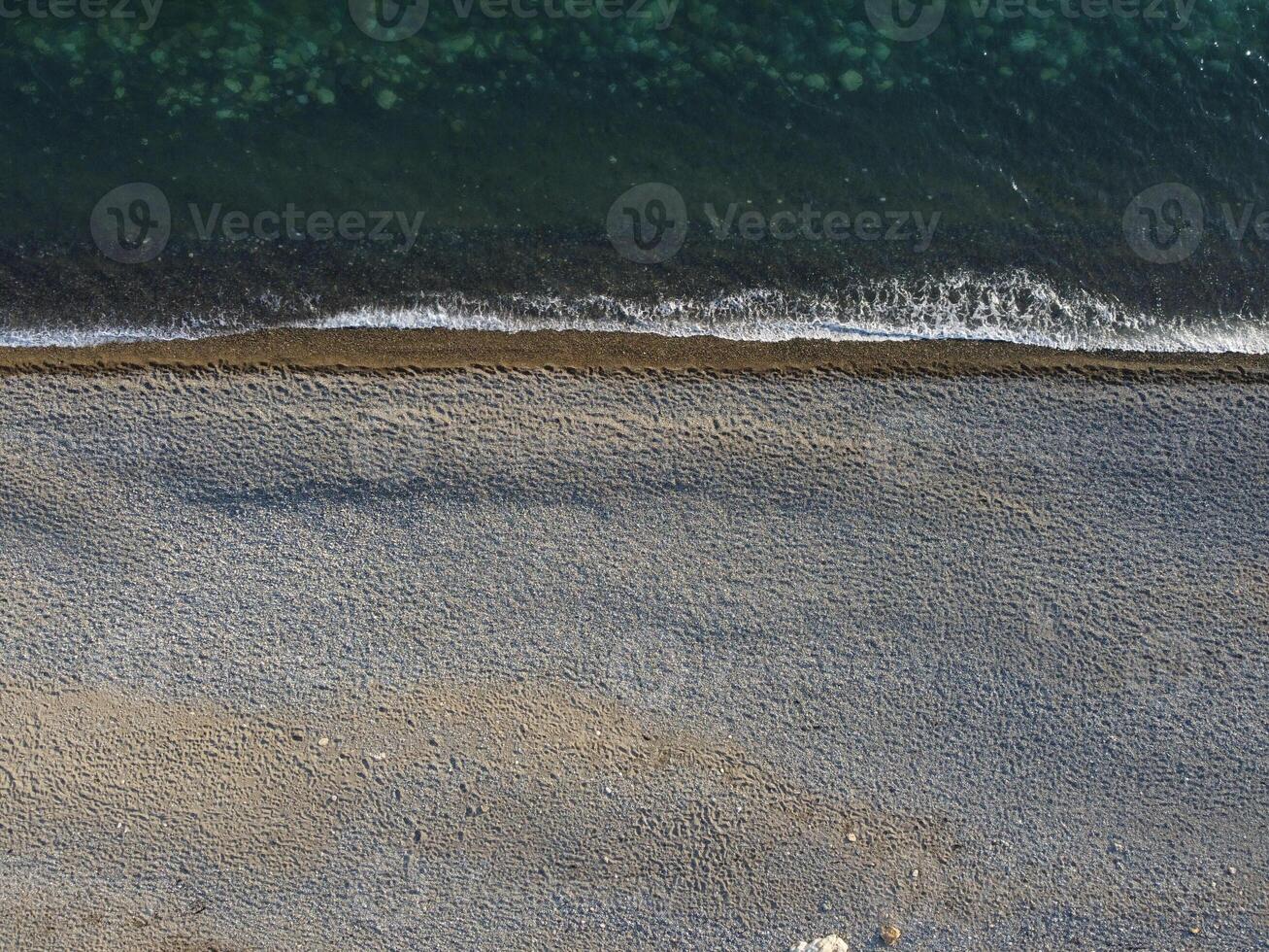 Aerial view from above on azure sea and pebbles beach. Small waves on cristal clear water surface in motion blur. Nature summer ocean sea beach background. Nobody. Holiday, vacation and travel concept photo