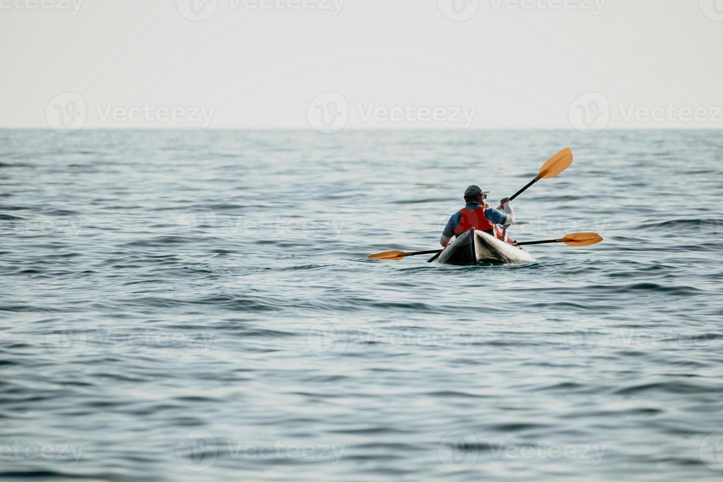 Happy couple kayaks in an inflatable kayak on the sea at sunset. Couple kanoeing in the sea near the island with mountains. People kayaking in life jackets sail. Back view photo