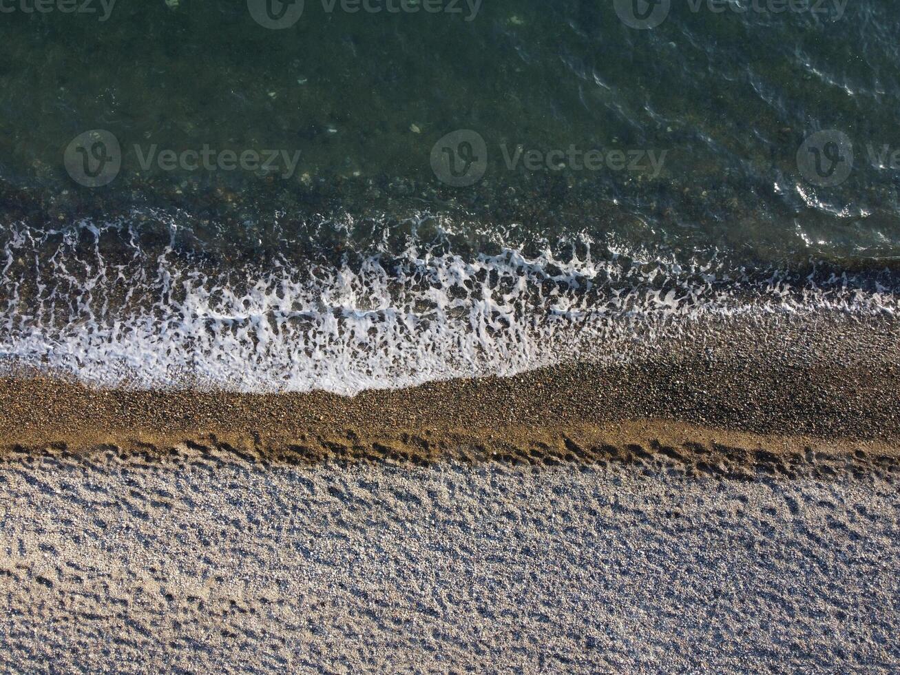 Aerial view from above on azure sea and pebbles beach. Small waves on cristal clear water surface in motion blur. Nature summer ocean sea beach background. Nobody. Holiday, vacation and travel concept photo