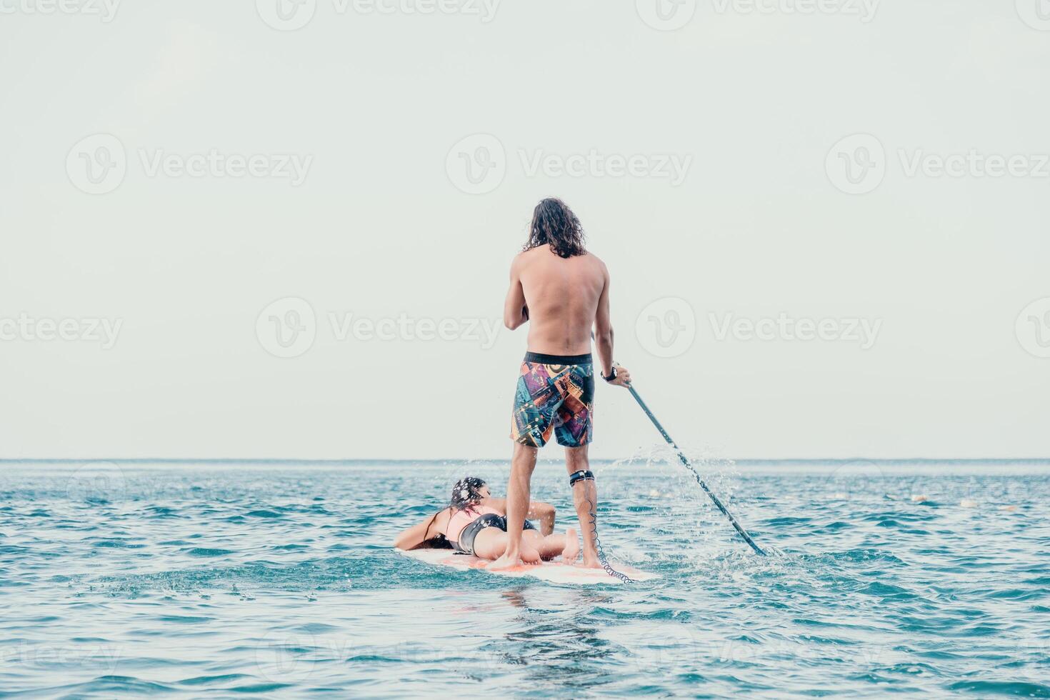Sea woman and man on sup. Silhouette of happy young woman and man, surfing on SUP board, confident paddling through water surface. Idyllic sunset. Active lifestyle at sea or river. Slow motion photo