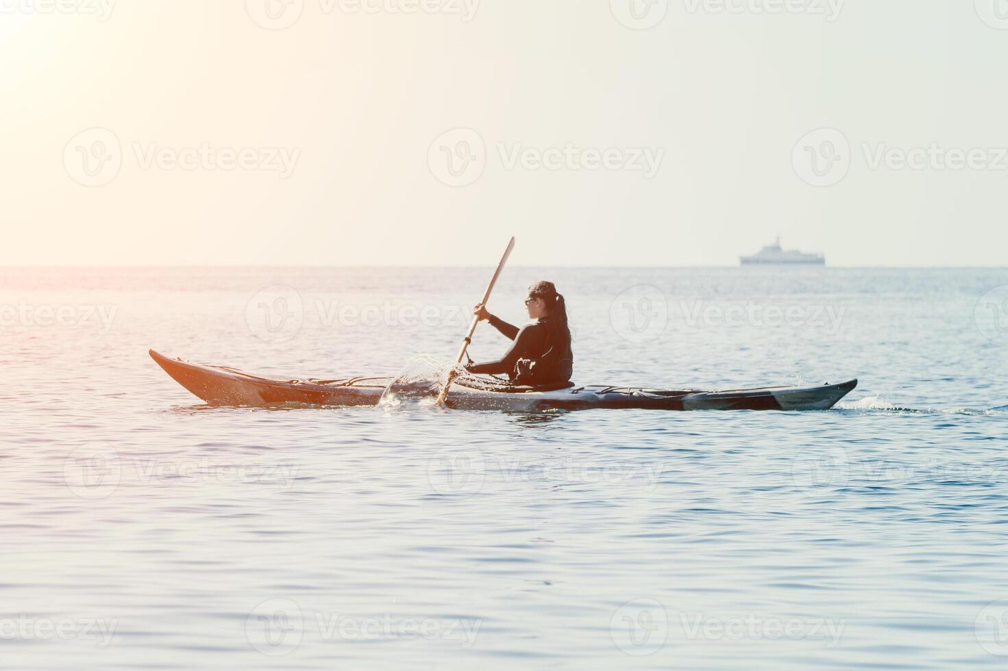 Woman sea kayak. Happy smiling woman in kayak on ocean, paddling with wooden oar. Calm sea water and horizon in background. Active lifestyle at sea. Summer vacation. photo